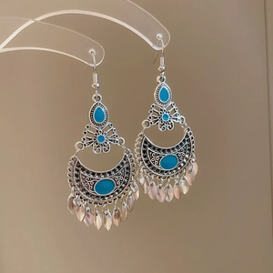 Detailed view of silver crescent earrings with blue enamel and leaf-shaped metal tassels