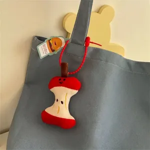 Cute apple core plush keychain in red and cream with bead chain on a grey canvas bag