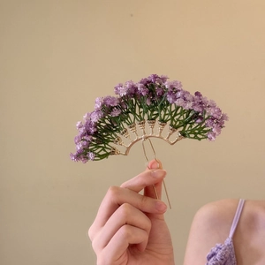 Detail view of a floral hair pin with purple silk flowers and golden U-shaped metal fork