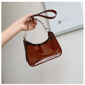 Detailed view of a transparent amber PVC baguette shoulder bag held against a white wall