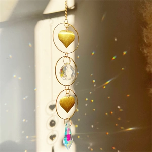 Macro view of crystal suncatcher with gold heart charms and rainbow light reflections