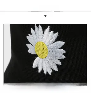 Close-up of a white daisy embroidery on a black cotton bucket hat with textured fabric