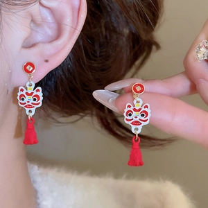 Gros plan sur les boucles d'oreilles lion chinois avec pompons rouges et émail doré