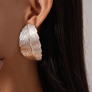 Macro view of large silver feather earring with brushed metal texture on model