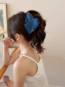 Gros plan d'une pince à cheveux en denim bleu brodée de cerises sur une queue de cheval