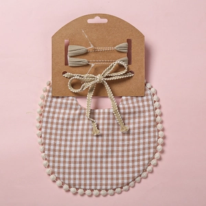 Détail d'un bavoir bébé avec bordure pompons et ensemble bandeau à motif écossais