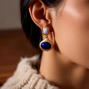 Vintage style gold earrings with blue water drop stones worn by a model in a beige sweater