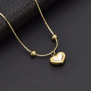 K-gold heart pendant necklace with white shell inlay and golden beads on a black background