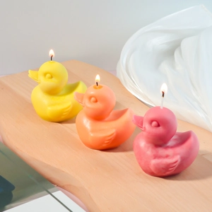 Three lit duck-shaped scented candles in yellow, orange, and pink on a wooden tray