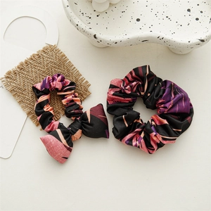 Flat lay of silk scrunchies with pink tropical leaf patterns and a chic ceramic tray