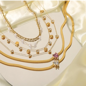 Detail of layered gold necklaces with shell, heart charms and pearls on champagne satin