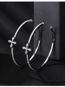 Macro side view of silver hoop earrings with zircon cross on black velvet background