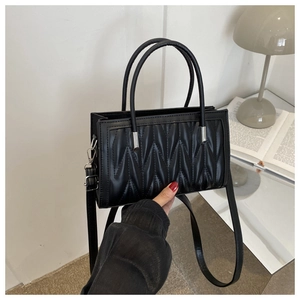 Detail of black PU leather handbag with quilted texture and metallic hardware accents
