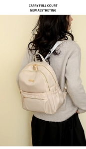 Beige nylon backpack with gold zippers and adjustable straps worn by a model