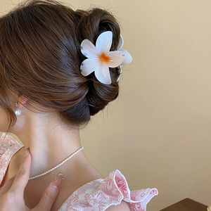 Floral hair claw clip with white petals and orange center styled on a chic bun hair