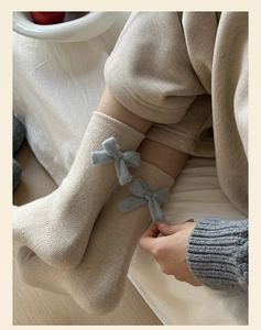 Close-up of beige wool knitted socks with 3D blue bow detail and soft texture