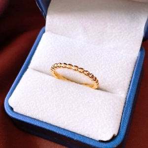 Detail shot of a gold-plated beaded ring featuring polished textured spheres on a blue stand
