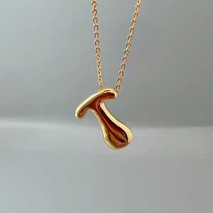 Macro shot of a polished golden T-letter pendant on a delicate metal O-chain necklace