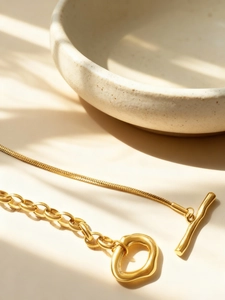 Detail of 18K gold-plated mixed chain necklace featuring a toggle clasp and leafy shadows