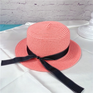 Detailed view of pink woven straw boater hat with black dotted ribbon embellishment