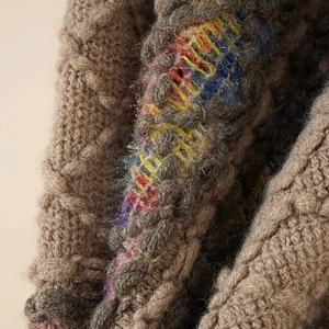 Detailed close-up of brown knit texture with rainbow patchwork on a wool poncho
