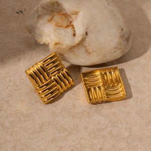 Macro shot of 18k gold plated stainless steel square textured earrings on white stone