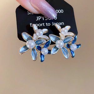 Macro view of 18K gold plated flower earring with blue enamel petals and white pearl center