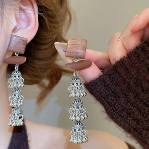 Détail de boucles d'oreilles ethniques en bois avec clochettes argentées superposées