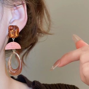 Detail of resin wood teardrop earrings featuring amber and pink layered segments on model