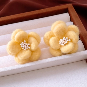 Detail view of yellow felt flower earrings with soft wool texture and white beaded centers