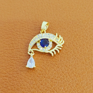 Detail of gold Evil Eye pendant with blue stone and teardrop crystal on brown leather