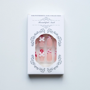 Detailed packaging of pink press-on nails with cherry designs, bows, and pearls