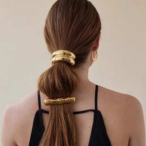 Detailed view of gold alloy hair clip and ponytail holder with hammered texture on model