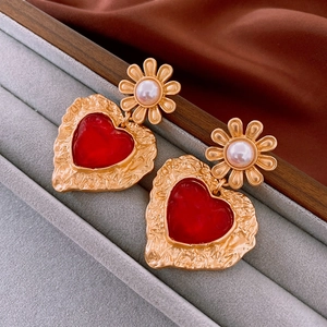 Detail of vintage gold flower earrings with red heart pendants on grey velvet tray