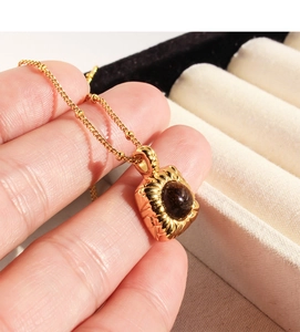 Close-up of golden square pendant with a deep brown gemstone held in hand over jewelry box