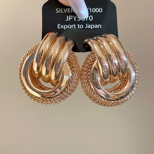 Détail de boucles d'oreilles dorées avec texture en maille tissée et design à boucles