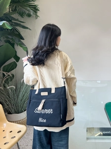 Lifestyle shot of large black canvas tote bag with beige straps worn over the shoulder
