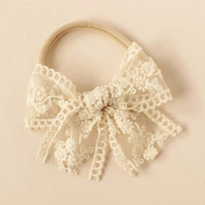 Detailed close-up of beige baby headband with intricate floral lace embroidery bow