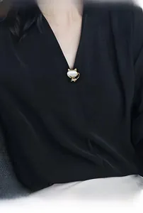 Detailed close-up of a golden cat brooch with opal stone on a black V-neck garment