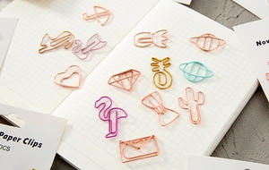 Variety of cute metal paper clips in rose gold and pink on a grid notebook