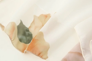 Detail of floral print chiffon dress showing orange watercolor flowers and rolled hem edges