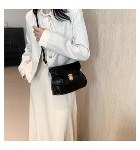 Detail of a pleated black leather shoulder bag with a gold buckle on an elegant model