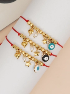 Close-up of four red woven friendship bracelets with evil eye and gold heart charms