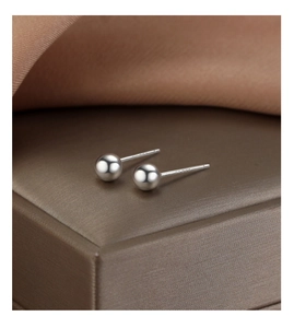 Macro shot of minimalist S925 sterling silver ball stud earrings on brown silk base