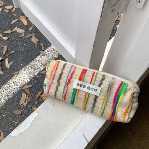 Detail of colorful striped fabric pouch with a small woven label against a wooden fence