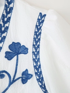 Close-up of blue floral embroidery on white crinkle cotton fabric of a bohemian top
