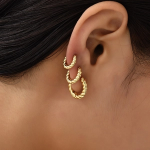 Three-piece set of golden twisted hoop earrings in various sizes on a female model