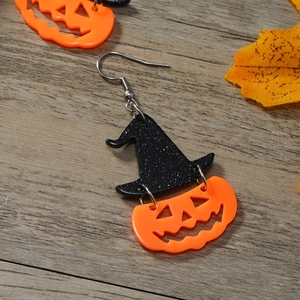 Macro detail of Halloween earrings with black witch hat and orange pumpkin on wood