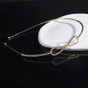 Elegant gold headband with rhinestone bow design shown on a sleek black mirror surface