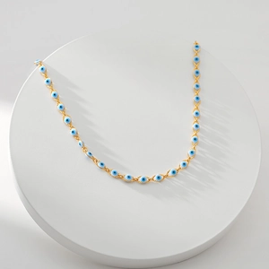 18K gold-plated Evil Eye necklace with blue enamel beads on a minimalist white tray